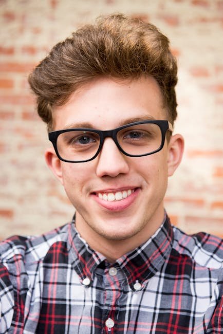 pexels-photo-769772-769772 Portrait of a smiling young man wearing eyeglasses and plaid shirt against a brick wall background.